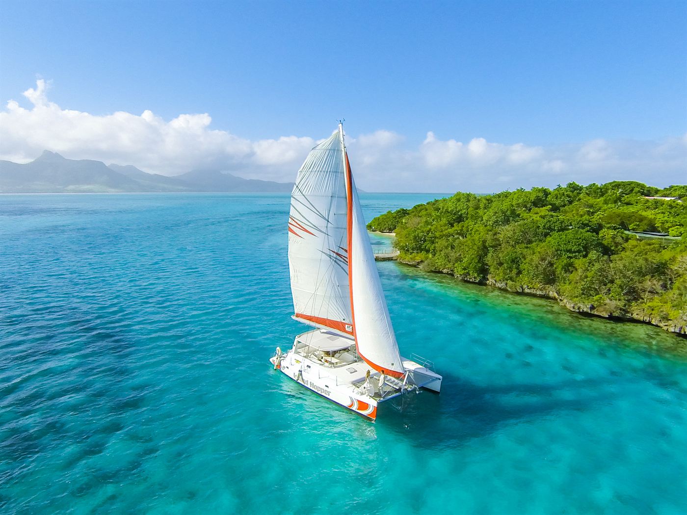 Catamaran toutes voiles dehors dans le lagon turquoise de l&rsquo;île Maurice, le long d&rsquo;un îlot boisé
