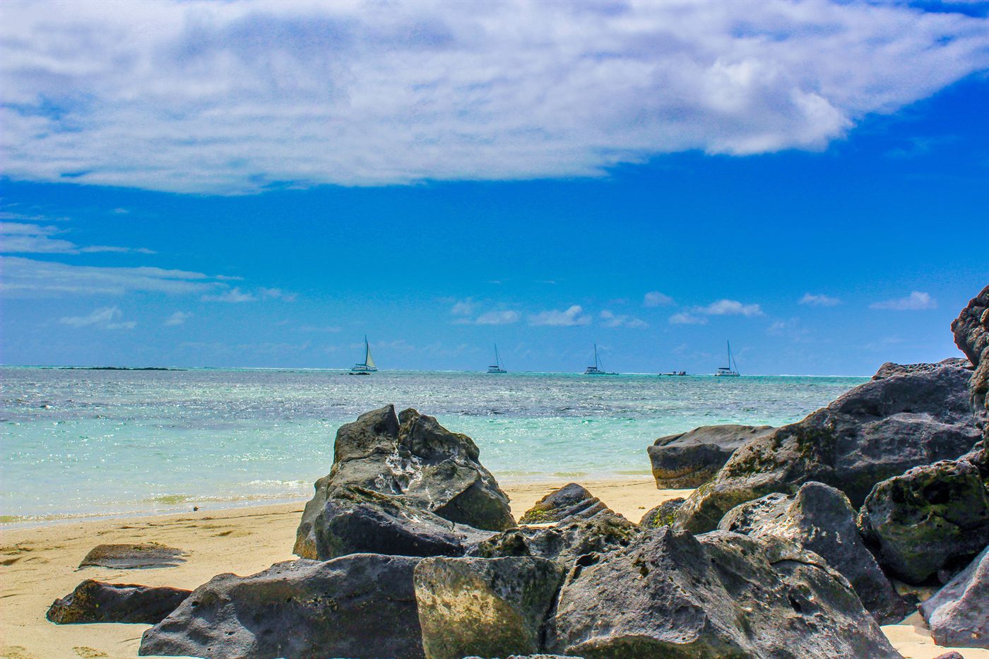 Catamarans au large d’une plage de l’île Maurice bordée de rochers volcaniques