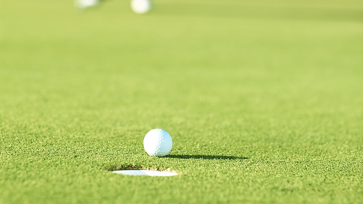 Balle posée au bord du trou sur un green, un joueur en approche à l&rsquo;arrière-plan