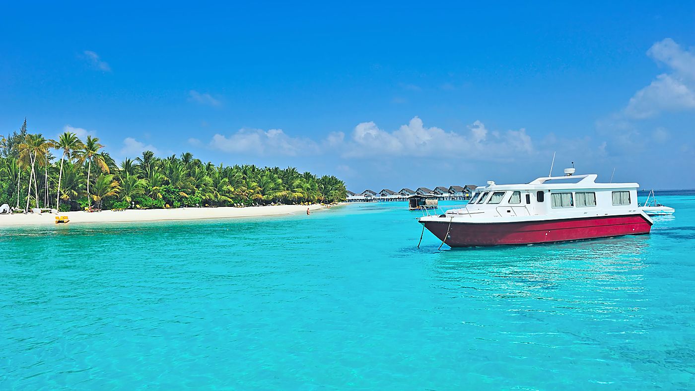 Îlot bordé de cocotiers et bateau au mouillage dans un lagon turquoise